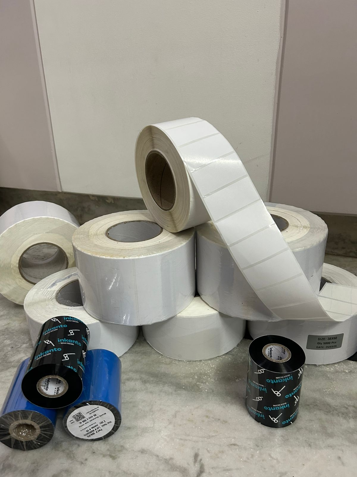 Blank label stock rolls stacked beside inkanto wax-resin ribbons